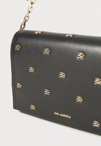 Black leather shoulder bag with gold-tone hardware and logo studs. Features a chain strap and smooth texture. Closed flap design.