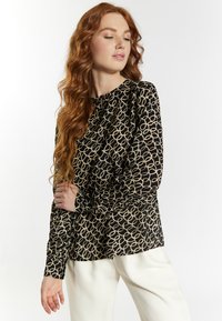 Blusa a maniche lunghe in tessuto nero con un motivo circolare beige, dotata di un collo rotondo e dettaglio con bottoni sul retro.