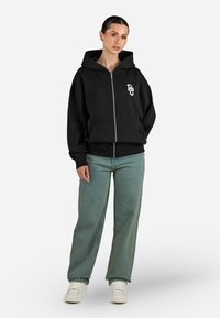 Felpa con zip nera realizzata in misto cotone, dotata di tasca frontale, cappuccio con coulisse e logo grafico bianco sul lato sinistro del petto.