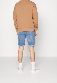 Sudadera marrón, pantalones cortos de mezclilla con los dobladillos enrollados, calcetines blancos y zapatillas informales. El conjunto tiene un ajuste relajado y un diseño sencillo.