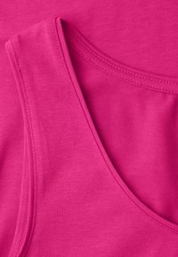 Gros plan de deux débardeurs en coton rose vif superposés montrant les coutures et la texture du tissu.