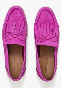 Rosa mockasiner i mocka med fransdetaljer och en rosett på ovansidan. Vit gummisula och små nitar på klacken. Modernt design.