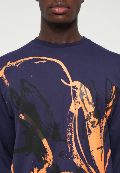 Navy long-sleeve shirt made of cotton, featuring an abstract orange and black graphic design across the front. Smooth texture and crew neckline.