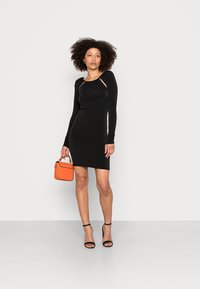 Vestido preto de manga longa com decote franzido e recortes, silhueta justa. Combinado com uma bolsa laranja de alça curta.