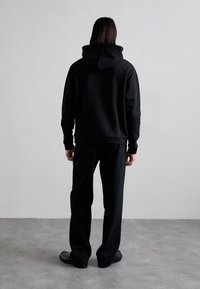 Czarna bluza z kapturem wyposażonym w sznurki, ściągacze przy rękawach i u dołu, zestawiona z pasującymi czarnymi spodniami dresowymi oraz gładkimi czarnymi butami.