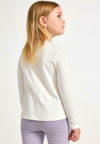 Langærmet, cremetop lavet af blødt bomuldsstof. Simpelt design med en rund halsudskæring, parret med lyse lilla teksturerede leggings.