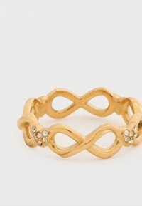 Χρυσό δαχτυλίδι με μοτίβο άπειρου, με υφή επιφάνειας και διακοσμητικά μικρών διάφανων στρας στη μία πλευρά.