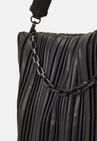 Zwarte geplooide leren tas met een gestructureerd oppervlak, voorzien van een kettingstrap en een gladde bovenkant. Het beslag is zwart met een glanzende afwerking.