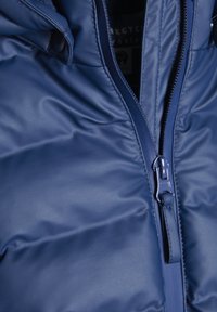 Marinblå puffjacka med framslående dragkedja, synliga sömmar och en slät, glansig yta. Designad med återvunna polyester-material.