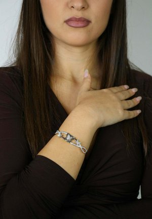 Bracelet en argent avec motifs de papillon et de fleur, orné de pierres claires. Porté au poignet d'un modèle avec un haut sombre.