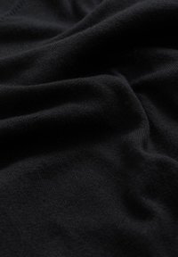 Svart stickad tyg med en mjuk, texturerad yta; slät falla skapar mjuka, flödande veck utan några mönster eller synlig hårdvara.