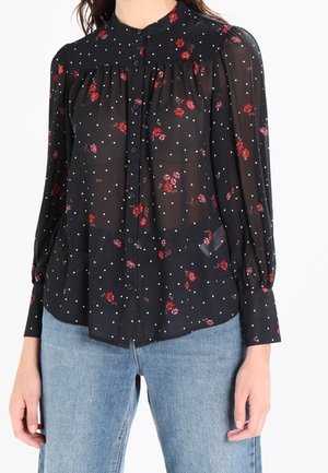 Musta läpikuultava paita, jossa punainen kukkakuosi ja valkoisia pilkkuja, pitkät puhvimaiset hihat, napillinen edusta, yhdistetty vaaleansinisiin farkkuihin.