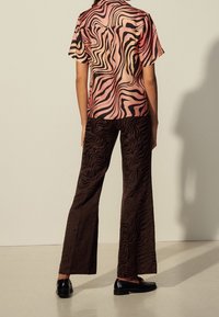 Chemise à manches courtes avec un motif ondulé rose et noir, associée à un pantalon large marron présentant un imprimé zèbre texturé. Des chaussures noires complètent le look.