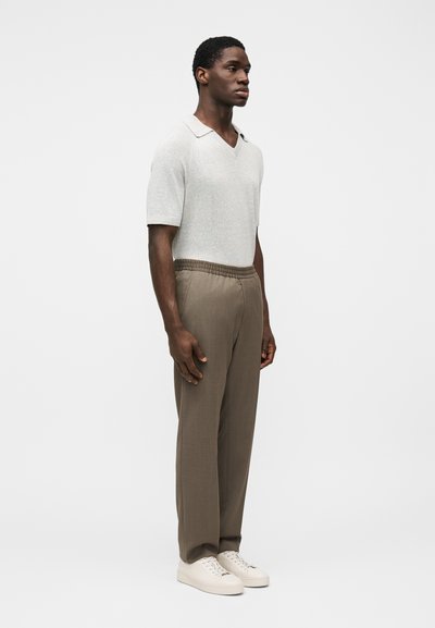 Πλεκτό πόλο μπλουζάκι με κοντά μανίκια σε ανοιχτό γκρι χρώμα και V-λαιμόκοψη, συνδυασμένο με μπεζ παντελόνια με ελαστική μέση και λευκά αθλητικά παπούτσια.