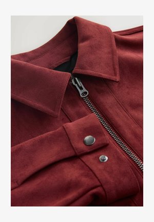 Sarkanvīna krāsas teksturēta jaka ar rāvējslēdzēja aizdari priekšpusē, lielu apkakli un spiedpogām. Pievērojami sudraba krāsas rāvējslēdzēji un metāla detaļas.