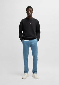 Un sweat noir avec le logo "BOSS", un pantalon bleu et des baskets blanches. Tissu lisse, coupe standard et design décontracté. Style minimaliste.