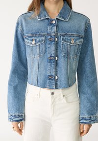 Kratka denim jakna v svetlo modri barvi s klasičnim ovratnikom, sprednjim gumbom, dvema žepoma na prsih in kontrastnim šivanjem.