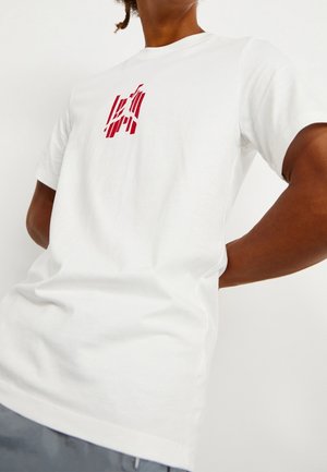 Weißes Baumwoll-T-Shirt mit rotem Grafikdesign auf der linken Brustpartie, mit rundem Ausschnitt und kurzen Ärmeln.