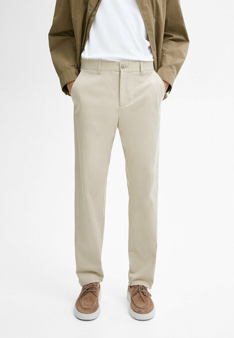 Beige trousers with a smooth texture, straight cut, and side pockets, paired with brown suede shoes and a white shirt underneath a brown jacket.
