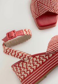 Crvene pletene platforme sandale s uzorkom križanja, s teksturiranim gornjim dijelom od tkanine i podesivim remenom oko gležnja sa kopčom.