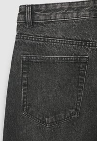 Tessuto di denim nero con finitura strutturata, con una tasca posteriore. Il bordo superiore presenta un leggero sfilacciamento e le cuciture sono di un grigio più chiaro.