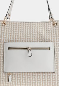 Sac fourre-tout tissé beige avec une poche avant en cuir blanc lisse, ornée d'une fermeture éclair et de matériaux dorés. Deux anses noires attachées.