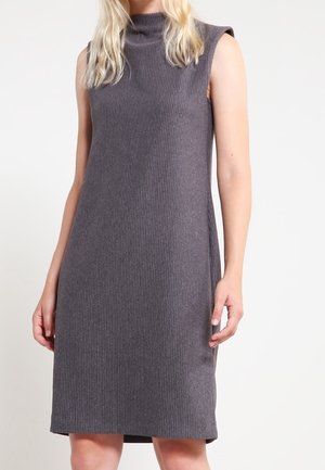 Bez rękawów, dzianinowa sukienka do kolan w ciemnoszarym kolorze z wysokim dekoltem, noszona przez osobę o długich blond włosach.