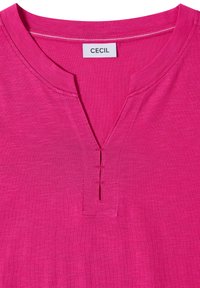 Chemise rose vif avec un col en V orné de surpiqûres décoratives et une étiquette blanche portant la mention CECIL au col.