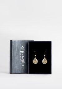 Orecchini d'oro con design floreale intricato, esposti in una scatola foderata in velluto nero con un logo argentato su una copertura grigia strutturata.