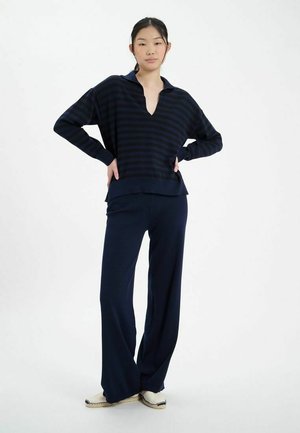 Pull en maille rayé marine avec col, associé à un pantalon large marine et des chaussures à enfiler crème. Texture douce en tricot tout au long.