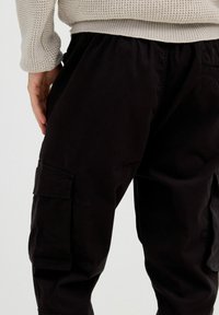 Los pantalones cargo negros presentan un corte holgado, cintura elástica, bolsillos laterales y una textura suave, adecuados para un uso informal.