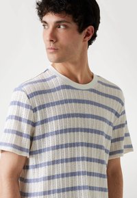 Camiseta de punto a rayas en blanco y azul claro, con textura acanalada, mangas cortas y cuello redondo con un ribete en contraste.