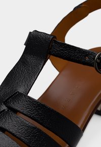 Μαύρο δερμάτινο σανδάλι με πολλαπλούς ιμάντες και στρογγυλό πόμολο. Διαθέτει λείο ταμπά εσωτερικό πέλμα με εγχάρακτο λογότυπο. Σχεδιασμός με επίπεδη σόλα.