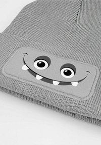 Gray knit beanie with a textured surface featuring a rectangular patch displaying a smiling monster design with large eyes and jagged teeth.