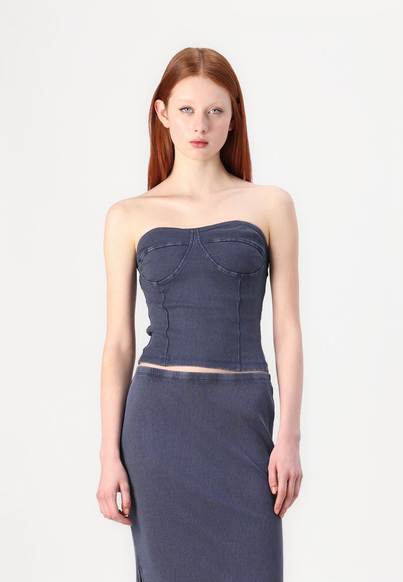 Top in denim senza spalline di colore blu scuro con un corpo aderente, texture a coste e dettagli di cucitura curvi. Abbinato a una gonna coordinata.