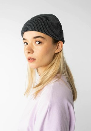 Grijze geribbelde beanie, snugly op het hoofd, gecombineerd met een lichtpaarse t-shirt. Haar is lang en steil, vallend over de schouder.