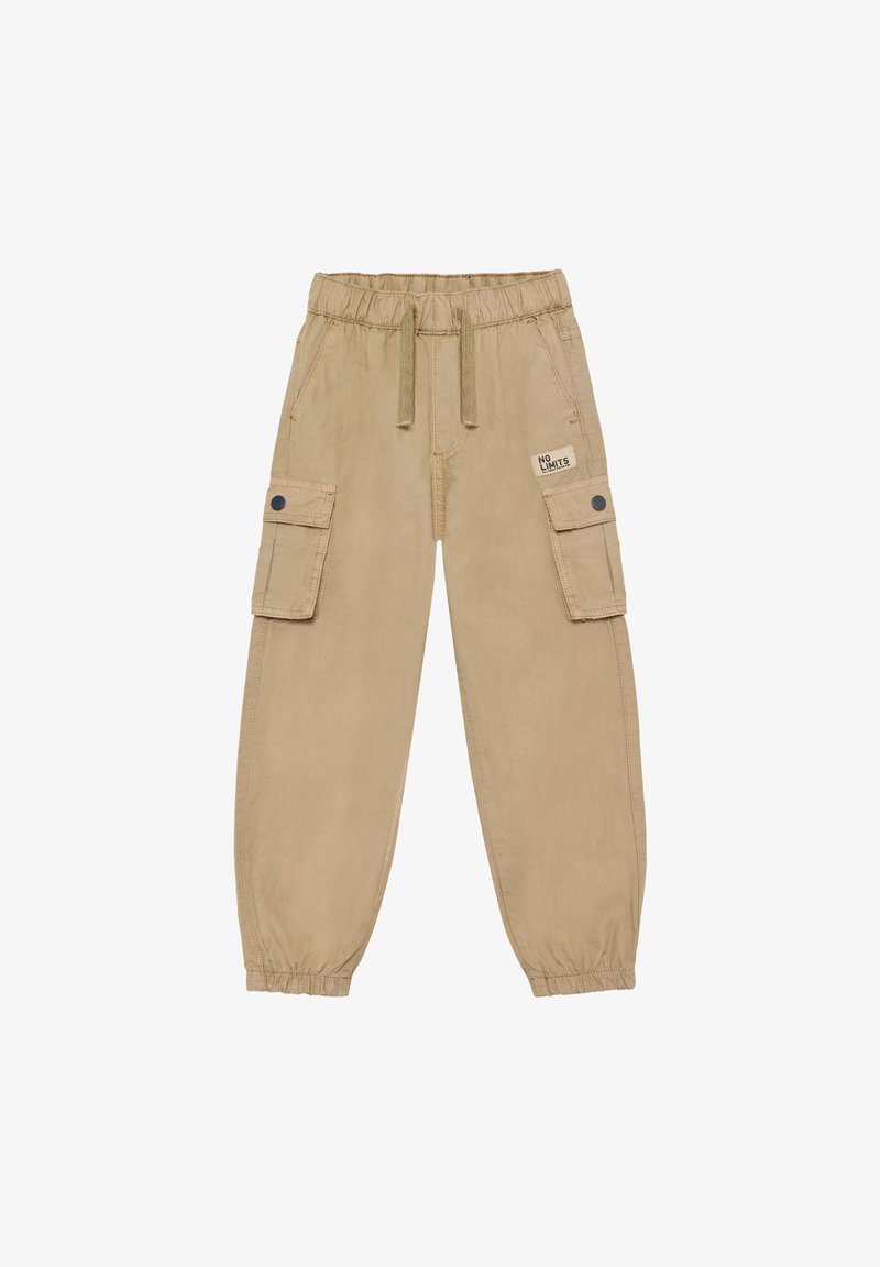 Pantalon cargo beige avec ceinture élastique, cordon de serrage, poches latérales à rabat avec boutons-pression et poignets élastiques, avec un patch "No Limits" sur la poche droite.
