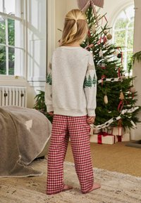 Grå sweatshirt med grønne trægrafikker, parret med rød og hvid ternet natbukser. Barnets ryg vender mod os, indendørs juleindstilling.
