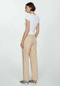 Wit korte mouwen aansluitend topje, beige wijde broek met achterzakken en groene hakken sandalen. Glad materiaal en casual ontwerp.