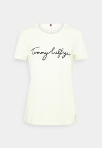 T-shirt en coton jaune clair à manches courtes avec un logo noir écrit à la main "Tommy Hilfiger" sur le devant, col rond.