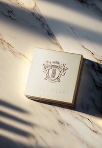 Bobbi Brown Kompakt mit einem cremefarbenen Äußeren, strukturiertem Logo und Wappen-Design, das erhabene Details und goldene Akzente aufweist.