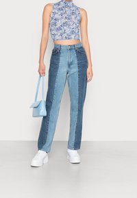 Blå blommig crop top med hög halsringning kombinerad med högmidjade, färgblockerade denimjeans. Vita platåskor och en ljusblå handväska.