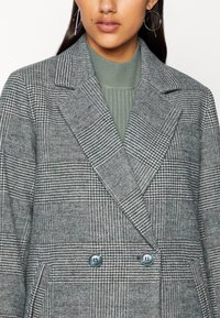 Szürke houndstooth mintás, dupla soros blézer, testre szabott kialakítással, széles hajtókákkal és kék gombokkal, textúrált anyagból készült.