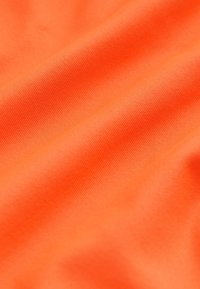 Tissu orange vif avec une texture subtile et des plis doux créant des ombres et des reflets délicats sur toute la surface.