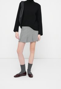 Suéter de cuello alto negro, falda plisada gris, calcetas acanaladas grises y zapatos planos de charol burdeos con lazos. Diseño y colores minimalistas.