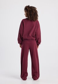 Bordeaux sweatshirt en broek set, gemaakt van zacht materiaal, met een losse pasvorm, verlaagde schouders en elastische boorden bij de polsen en enkels.