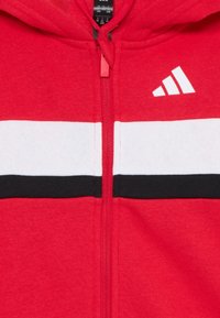 Red zip-up hoodie featuring a white and black stripe across the chest, with a white Adidas logo on the right side.