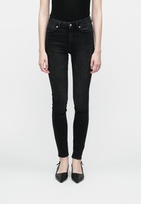 Jeans skinny pretos com uma cintura de altura média, apresentando bolsos frontais e costura decorativa nas laterais. O material é denim.