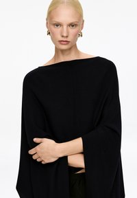 Schwarzer gestrickter Poncho mit weitem Ausschnitt, lässiger Passform, weiten Ärmeln und glatter Textur. Einfaches Design ohne Muster oder Akzente.