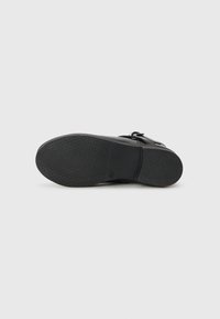 Sandale noire avec une semelle en caoutchouc texturée, dotée d'une large sangle et d'un accent en boucle. La chaussure a une surface supérieure lisse.